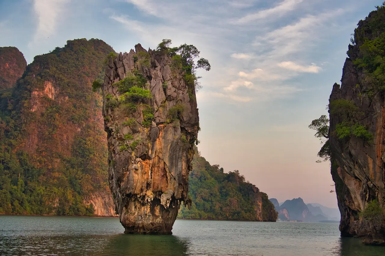 Free-standing limestone pinnacle rising from flat green water in Phang Nga Bay