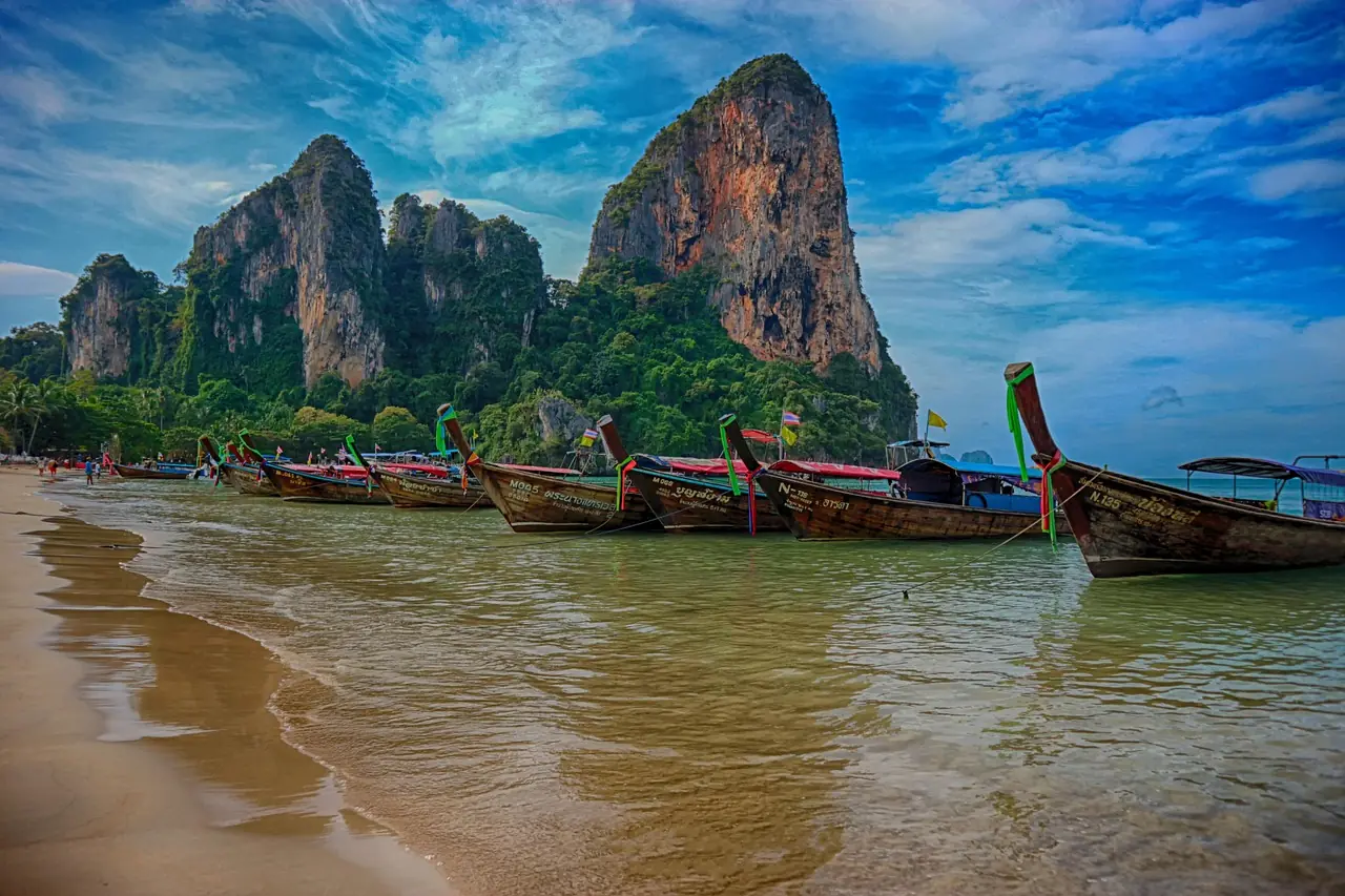 Beach enclosed by limestone cliffs with longtail boats moored off